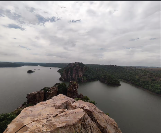 Panoramic view of Kandana Backwaters with blue-green water, tiny islands, and Aravalli hills.